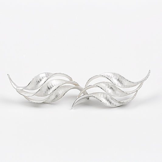 A pair of silver wedding earrings in the form of a triple wave of parallel curling, twisting S-shapes. They have a hammered texture, non-reflective surface and burnished edges. 