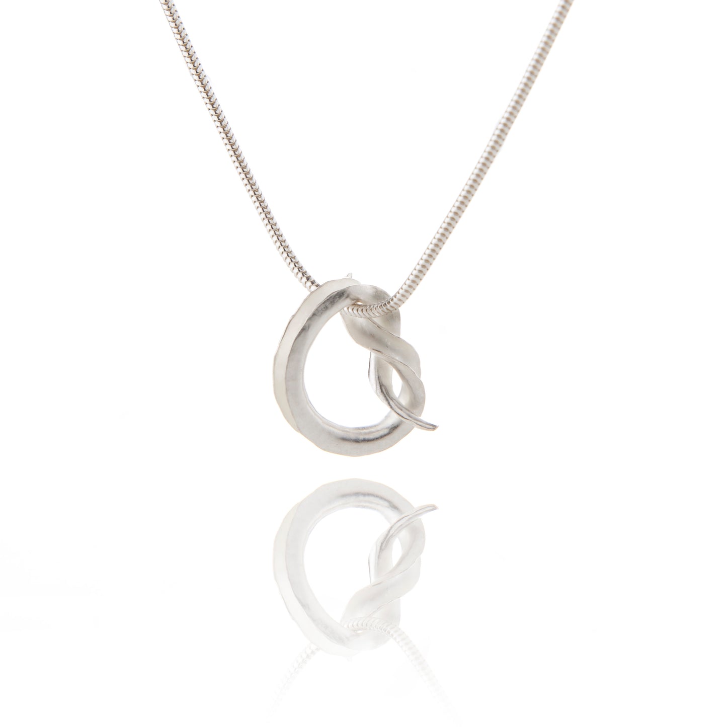 A silver pendant in the shape of a knot, in the form of a tube open down one side, hanging from a silver snake chain.