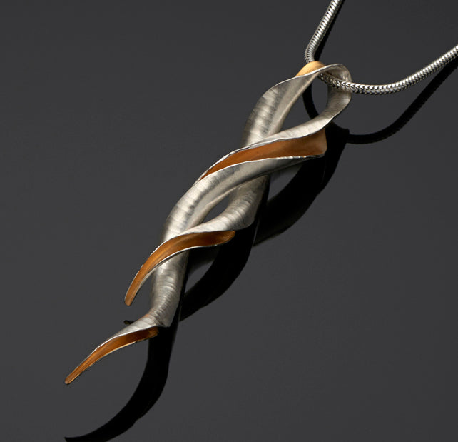 A silver pendant in the form of an open-sided tube, gold plated on the inside, with the two ends twisted around one another, leaving a loop for the snake chain to pass through.