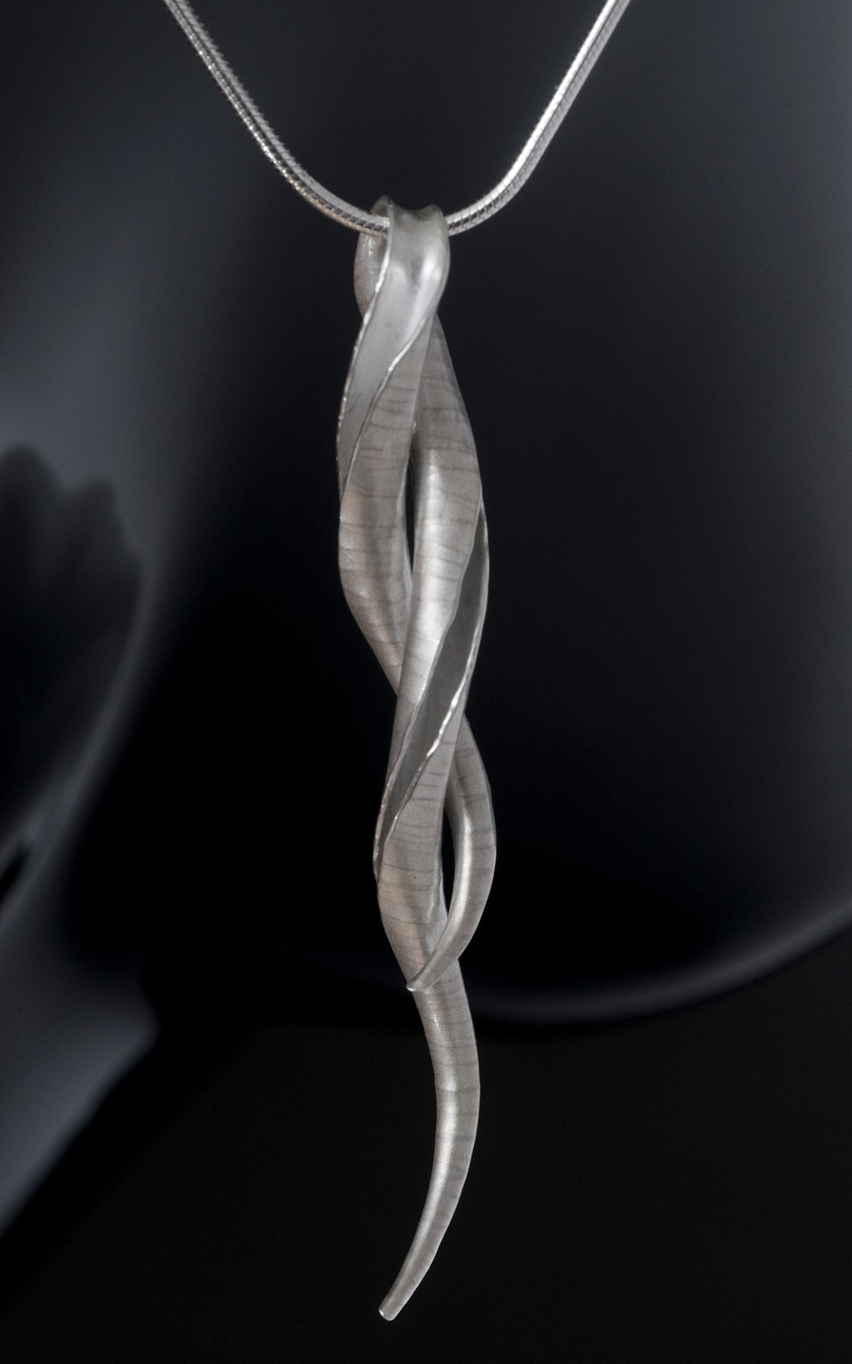 A silver pendant in the form of an open-sided tube, with the two ends twisted around one another, leaving a loop for the snake chain to pass through.